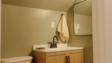 A bathroom with a toilet, sink, wooden cabinet, and a mirror.