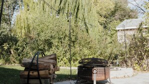 Un espace extérieur rustique, agrémenté d’un foyer en métal et d’une pile de bois de chauffage.