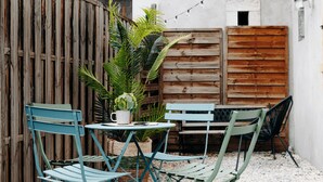 Un petit espace extérieur aménagé avec une table et des chaises, entouré de clôtures en bois et agrémenté d’une plante en pot.