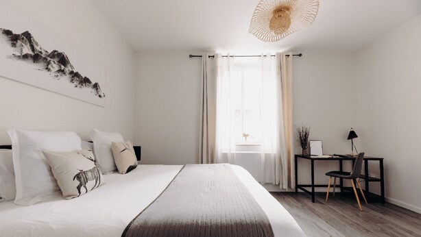 Une chambre à coucher au style minimaliste, avec un grand lit, un bureau et une fenêtre ornée de rideaux légers.