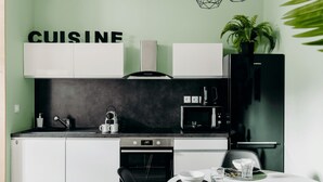 Une cuisine compacte avec des meubles blancs, un four encastré, une machine à café et un coin repas avec une table dressée pour deux personnes.