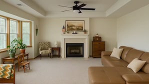 Een woonkamer met een open haard, een bank, een fauteuil, een tafel met een plant en een raam met jaloezieën.