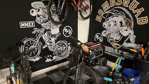 Een kamer met een zwart-wit geruit vloer, een muur met illustraties van motorfietsen en BMX-fietsen, en een rode BMX-fiets die aan de muur hangt.