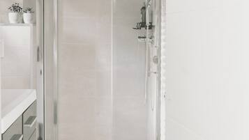 Une salle de bain moderne avec une douche à parois de verre, des carreaux blancs et une petite étagère ornée de plantes en pot.