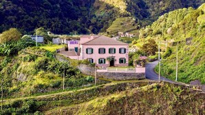 Eine pinkfarbene Villa mit Ziegeldach, umgeben von üppiger Vegetation und terrassierten Feldern.