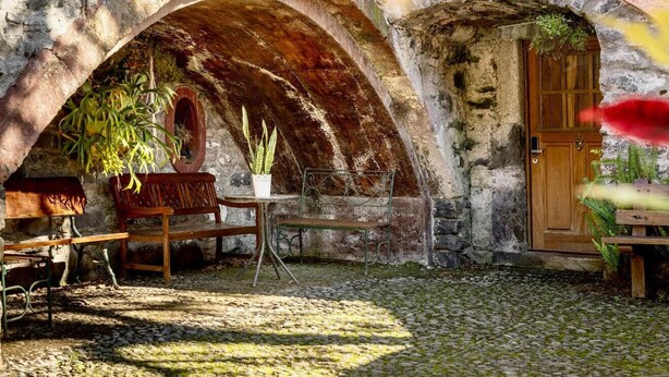 Ein rustikales Steinhaus mit Holztür, einer Bank und einem Tisch mit Blumentöpfen.