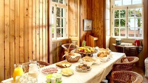 Ein Zimmer mit Holzwänden und reichhaltigem Frühstücksbuffet mit Brot, Gebäck, Früchten und Milchprodukten.