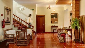 Eine Hotelhalle mit Treppe, Korbmöbeln, einer Holztür und einem Blumentopf.
