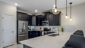 Une cuisine moderne avec des meubles de couleur sombre, des appareils en acier inoxydable, un îlot central et des luminaires suspendus.
