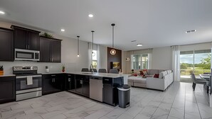 Une cuisine moderne avec des meubles de couleur sombre, un îlot central et un coin repas comprenant un canapé et une table.