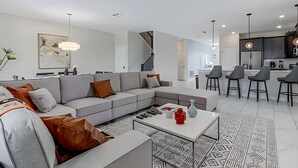 Un salon moderne avec un canapé d’angle, une table basse et un coin repas équipé de tabourets de bar.