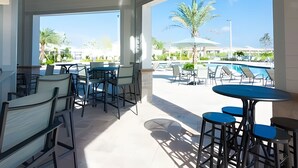 An outdoor patio area with tables and chairs, a pool, and palm trees.