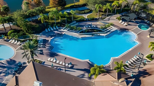 Luchtbeeld van een resort met een groot centraal zwembad, omgeven door loungegedeeltes en palmbomen.