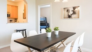 Een eetgedeelte met een donker houten tafel, witte stoelen en twee potten met planten.