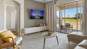 A modern living room with a flat-screen TV, a sofa, a coffee table, and a balcony with a view of the countryside. - 3BR Villa w/ Resort Access Near Disney (Davenport)
