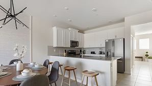 A modern kitchen with white cabinets, a stainless steel refrigerator, and a dining area with a round table and chairs. - 3BR Villa w/ Resort Access Near Disney (Davenport)