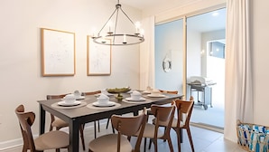Uma área de refeições com uma mesa retangular posta para seis pessoas, cercada por seis cadeiras. Há quadros emoldurados na parede acima da mesa.