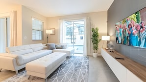 Uma sala de estar moderna com um sofá branco, uma televisão de tela grande e um tapete com padrão geométrico.