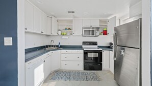 Une cuisine compacte avec des meubles blancs, un réfrigérateur en acier inoxydable, un four à micro-ondes, une cuisinière et un lave-vaisselle.