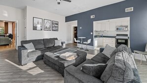Un salon moderne avec un canapé d’angle gris, une table basse et un coin repas avec des chaises blanches.