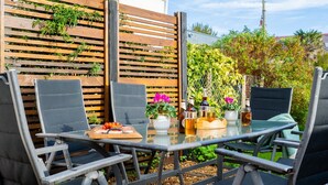 An outdoor patio with a glass table, two black chairs, and a wooden fence with plants. - Church House - sleeps 6 guests  in 3 bedrooms (Beaumaris)