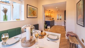 A dining area with a table set for two, featuring a bottle of wine, cheese, and bread. - Church House - sleeps 6 guests  in 3 bedrooms (Beaumaris)
