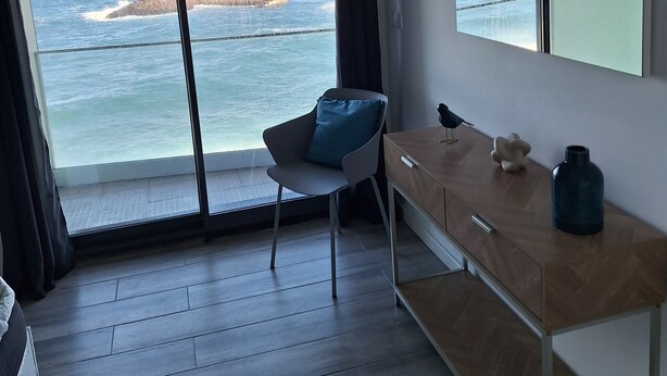 A modern room with a large window offering a view of the sea and rocky coastline.