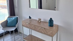 A modern room with a wooden console table, a chair with a blue cushion, a large mirror, and a view of the outdoors.
