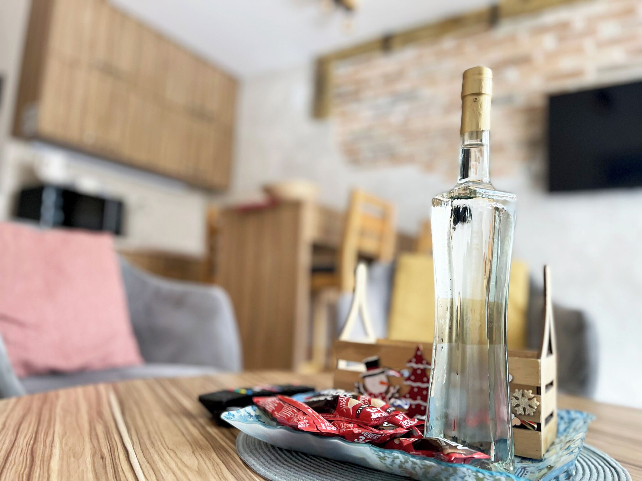 Una botella de vidrio transparente sobre una mesa de madera con un posavasos, rodeada de bombones envueltos.