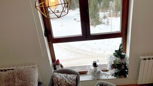 A room with a large window overlooking a snowy landscape, a small Christmas tree, and a decorative snowman. - NPL Gorstak apartments (Jahorina)