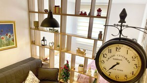 A cozy living room with a sofa, a coffee table, and a bookshelf. A clock is mounted on the wall, and a small Christmas tree is visible. - NPL Gorstak apartments (Jahorina)