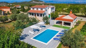 En villa med swimmingpool, omgivet af grønt og med et bjergrigt baggrundslandskab.