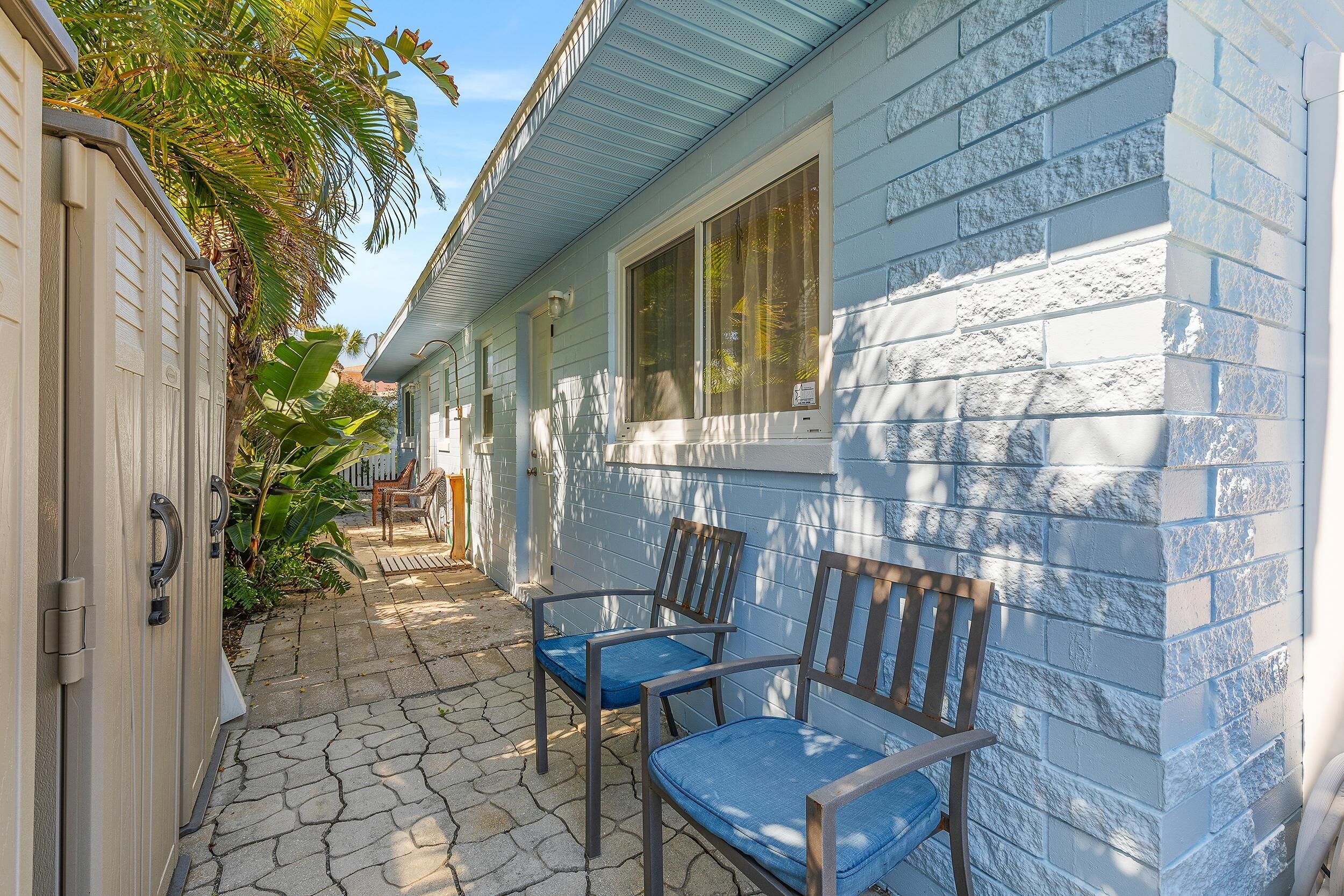 A house with a blue exterior, a covered patio with two wooden chairs, and a small garden area.