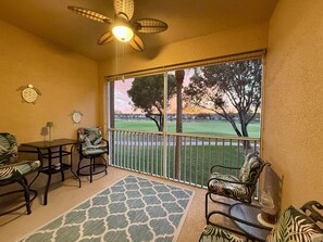 Ein Balkon mit Blick auf einen Golfplatz, ein Deckenventilator und ein Tisch mit Stühlen.