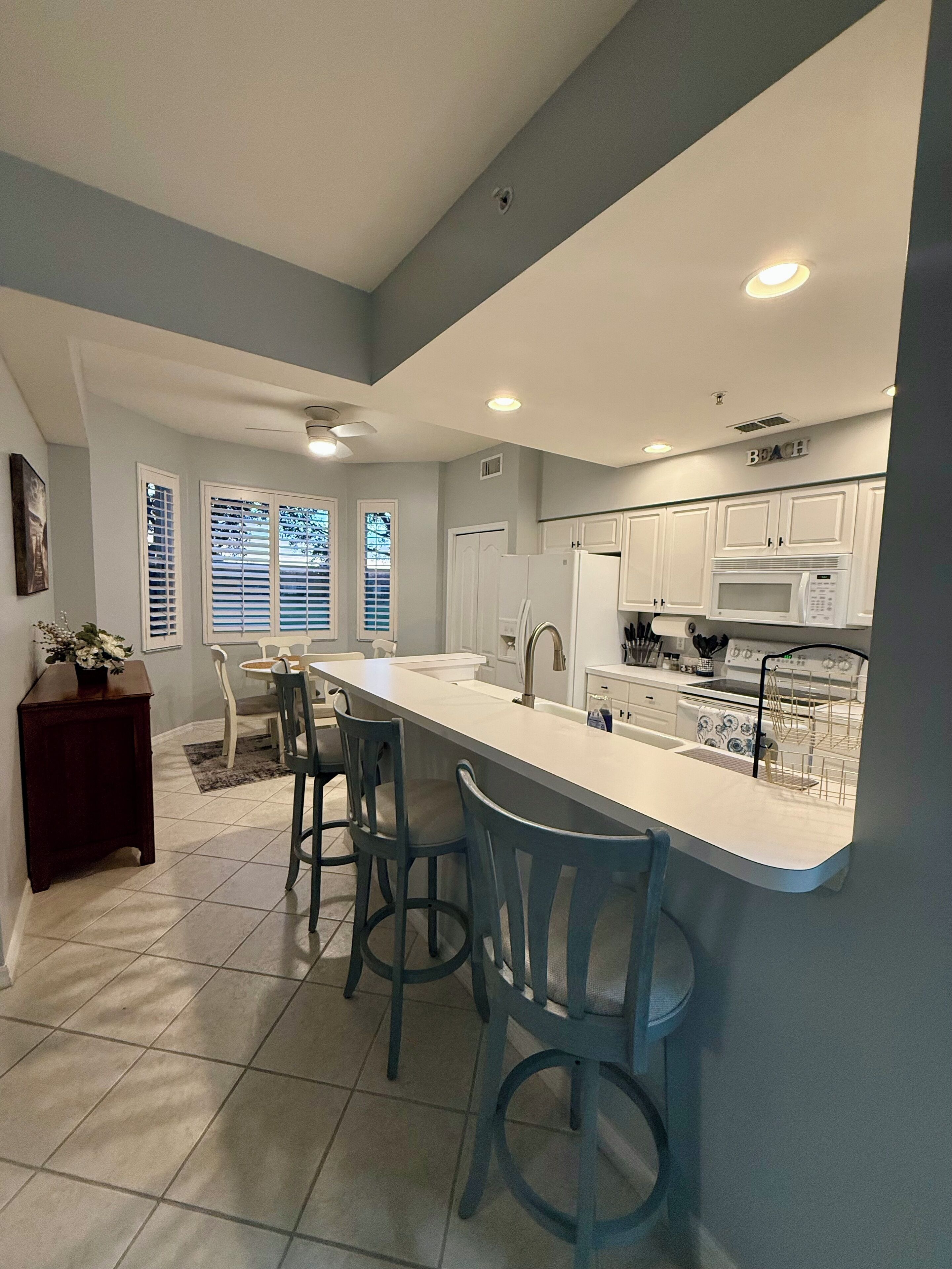 A modern kitchen with white cabinets, a large island with bar stools, and a built-in microwave.