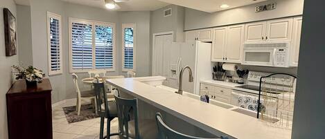 A modern kitchen with white cabinets, a large island with bar stools, and a built-in microwave.