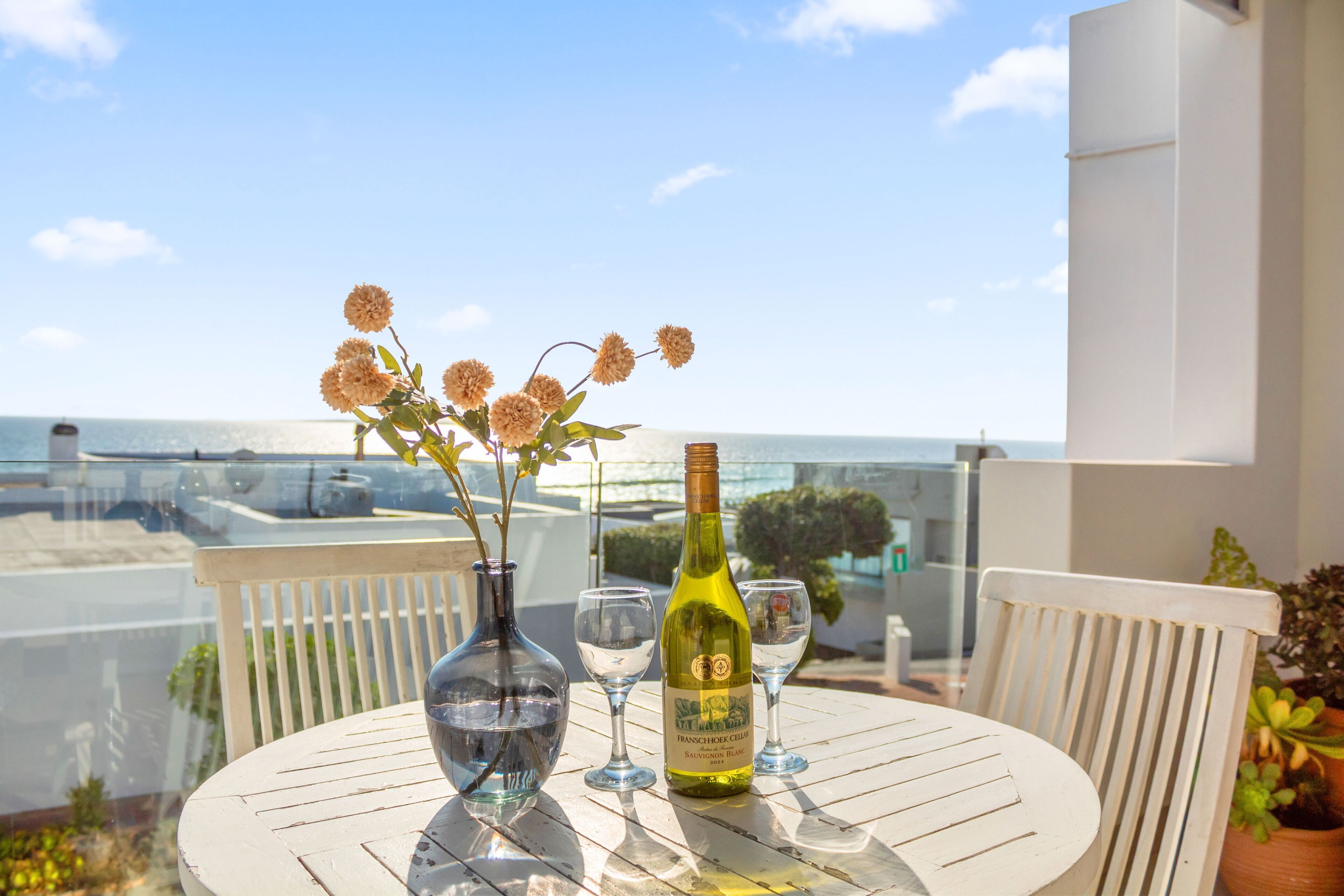 Een ronde tafel met een fles wijn, een glas en een vaas met bloemen.
