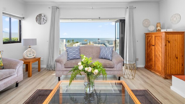 A modern living room with a sofa, a coffee table with a vase of flowers, and a view of the sea through large windows. - 19 Ascension (Cape Town)