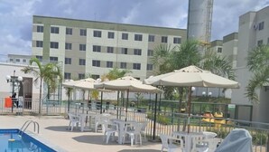 Une piscine entourée d’une clôture et de palmiers, avec des chaises longues blanches et des parasols.
