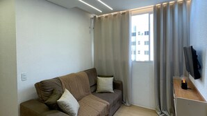 Un salon moderne avec un canapé, un téléviseur à écran plat et une fenêtre avec des rideaux.