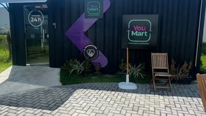 L’entrée d’un magasin YouMart, avec une enseigne indiquant un service ouvert 24 heures sur 24, une flèche violette et une chaise en bois à l’extérieur.