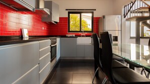 A modern kitchen with red tiles, a window, and a dining area with chairs. - Skyline Villas Top - Fantastic sea view (Calheta)