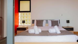 A neatly made bed with rolled towels, a bedside table with a lamp, and a window with a view of greenery. - Skyline Villas Top - Fantastic sea view (Calheta)