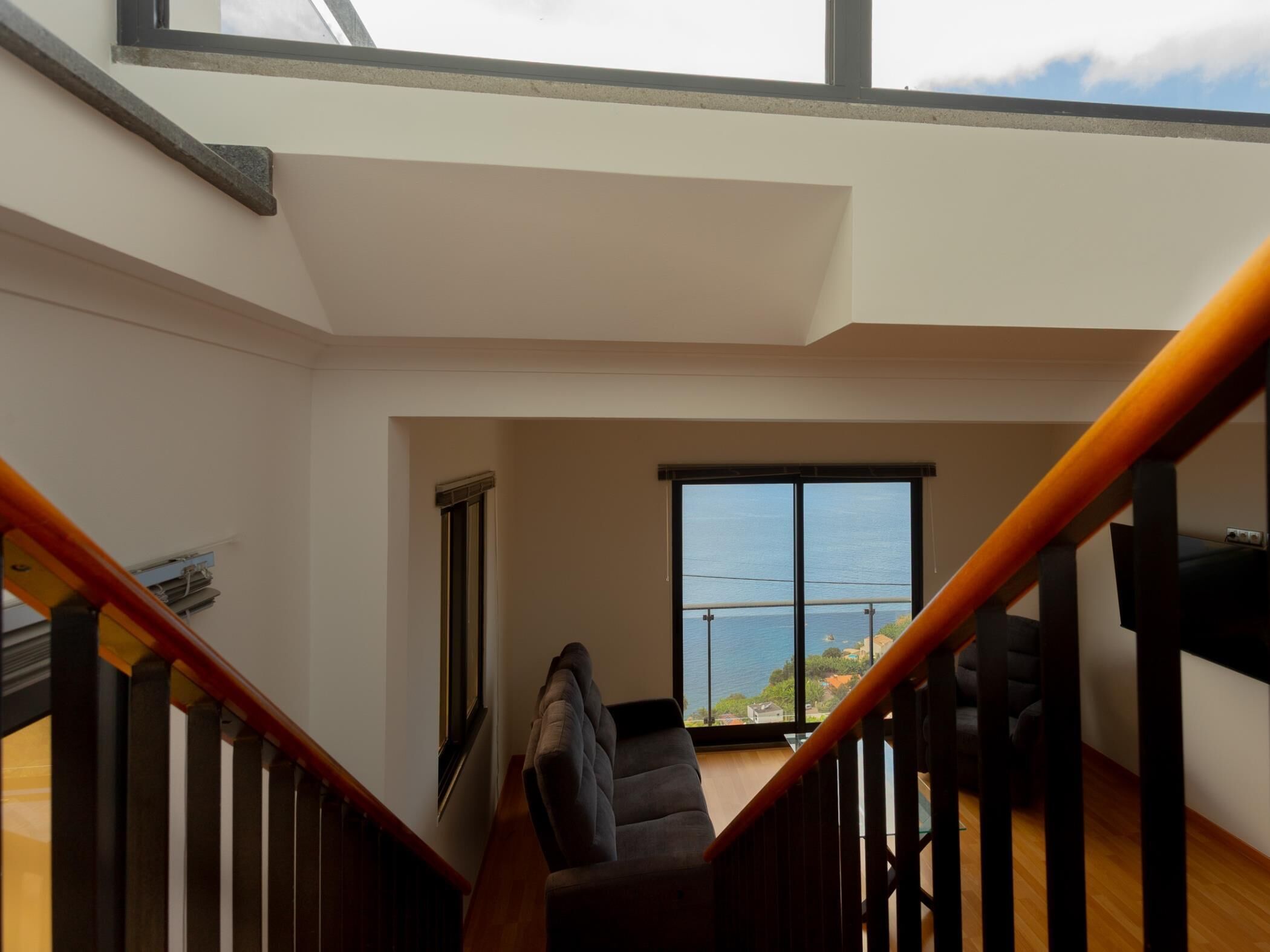 A spacious room with a large window offering a view of the sea, a wooden staircase, and a modern chair.