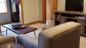 A cozy living room with a sofa, a coffee table, and a television on a wooden stand. - Keweenaw, Houghton/Hancock/MTU/Trails/Sauna (Houghton)