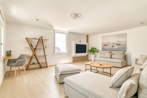 Un salon moderne avec un canapé, un pouf, une télévision et une étagère en bois en forme d’échelle.