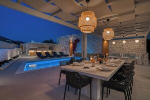 Ein gut beleuchteter Außenbereich zum Essen mit Pool, Steinmauern und modernen Lampen.