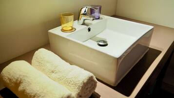 A bathroom with a white sink, a glass cup, and two rolled towels.