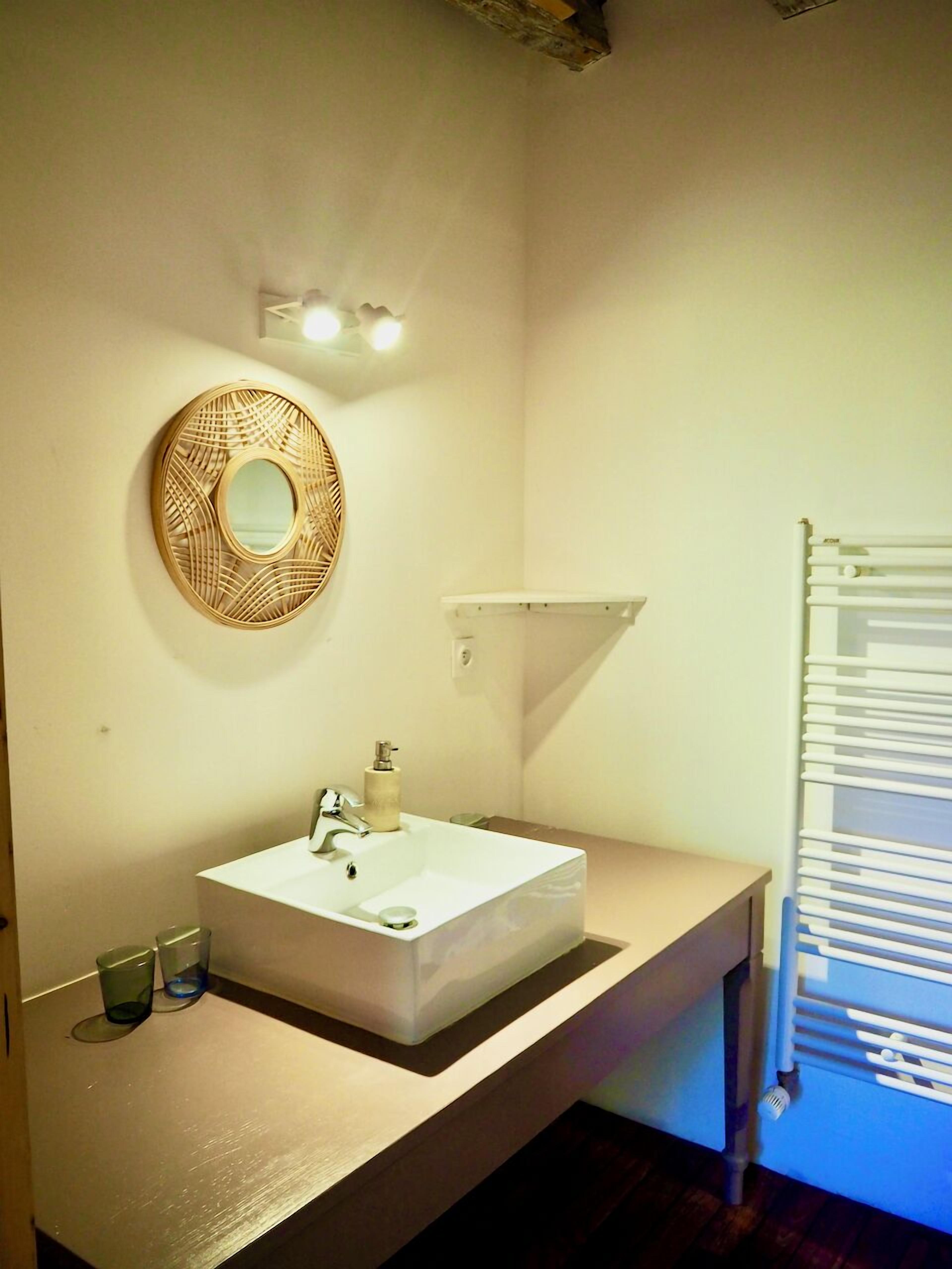 A bathroom with a white sink, a mirror with a decorative frame, a towel rack, and a shelf above the sink.