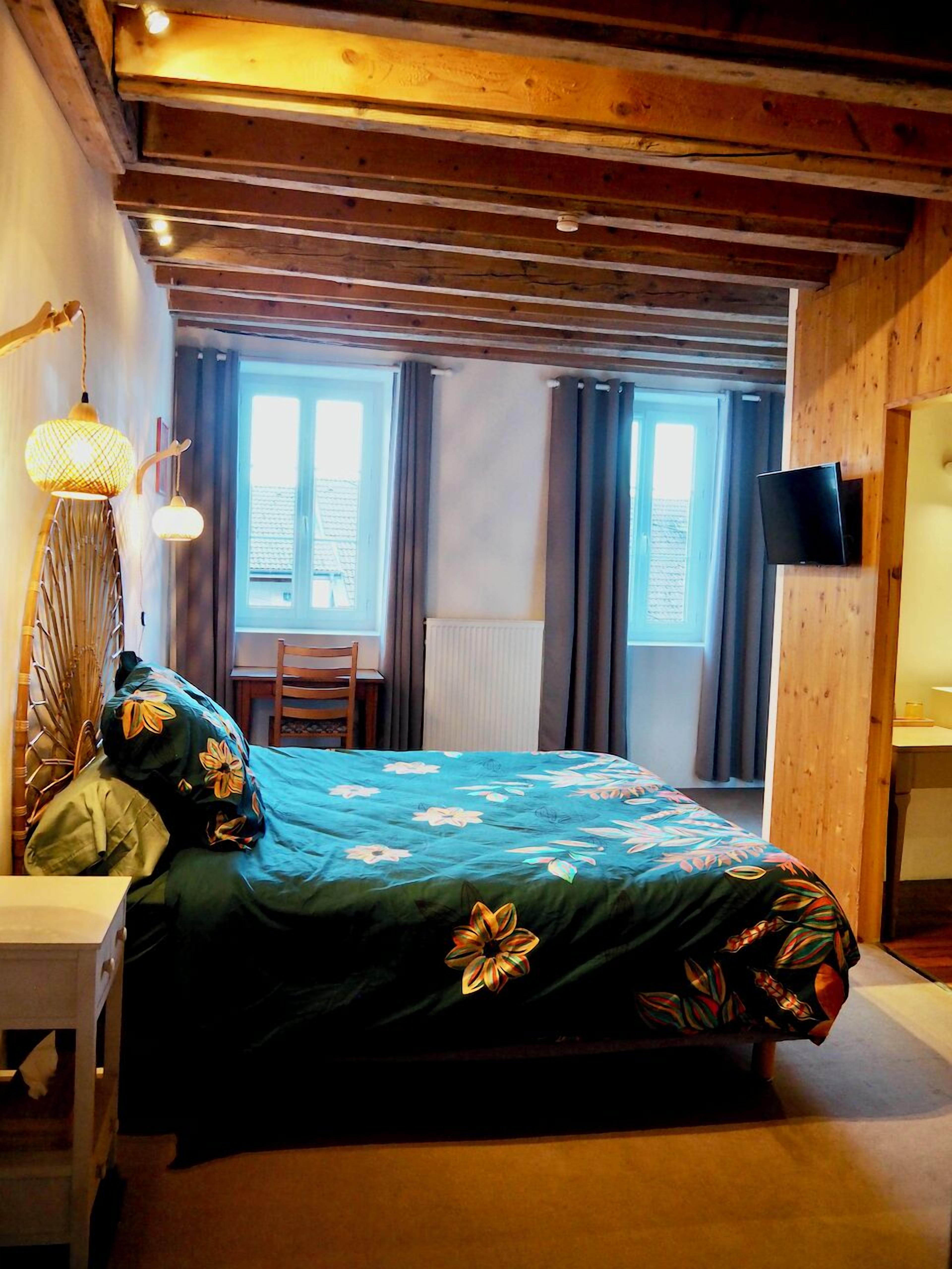 A bedroom with a bed, a desk, a chair, a TV, and a window with curtains.